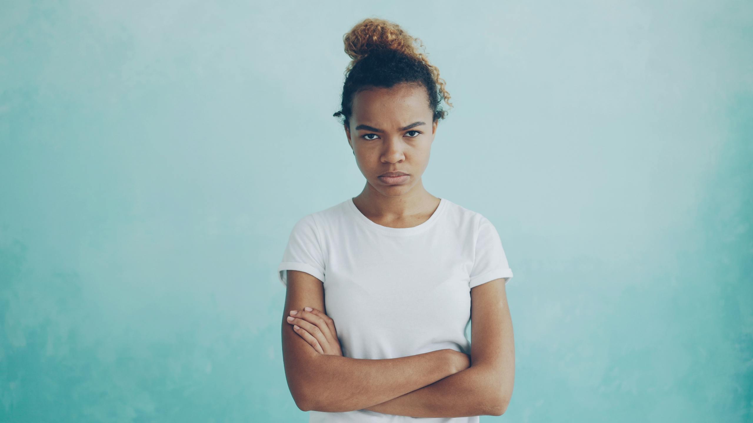 Portrait of a woman with an intense gaze and crossed arms, set against a blue background.