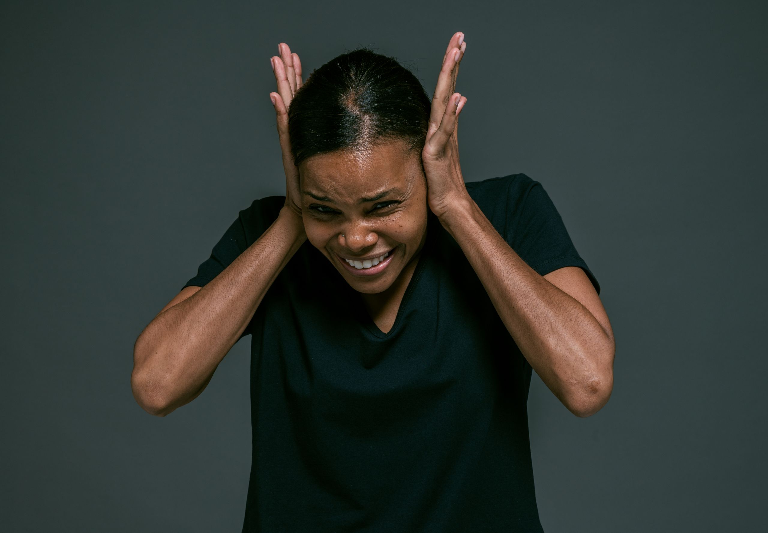 Portrait of an adult woman covering ears, looking irritated, against a dark background.