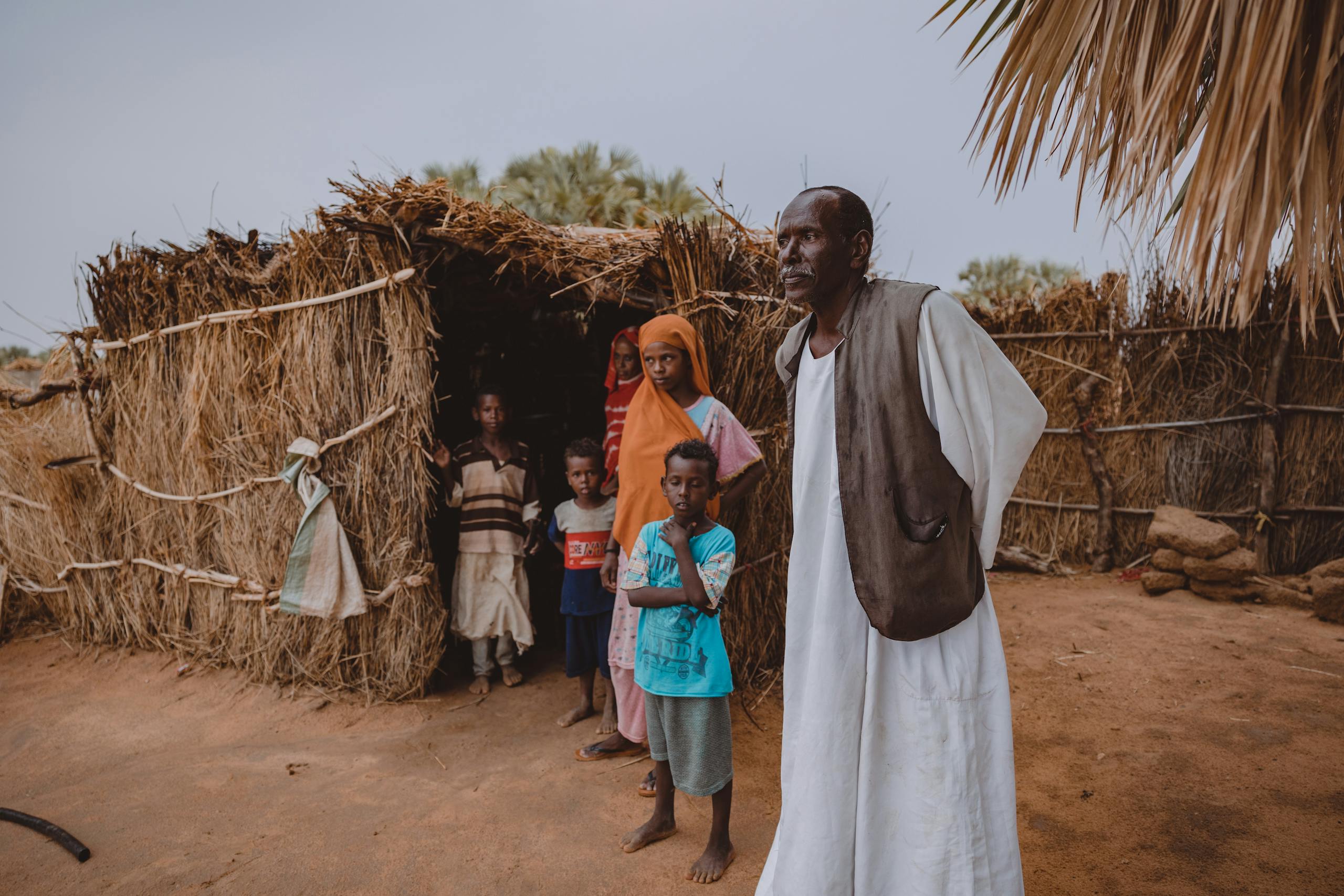 Portrait of family standing outside a traditional straw hut in a rural village.
