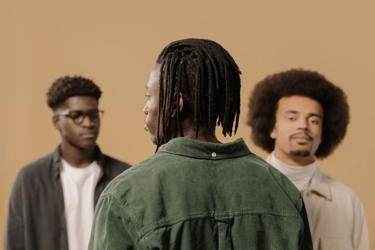 Portrait of three stylish men with diverse hairstyles in a studio setting against a brown background.