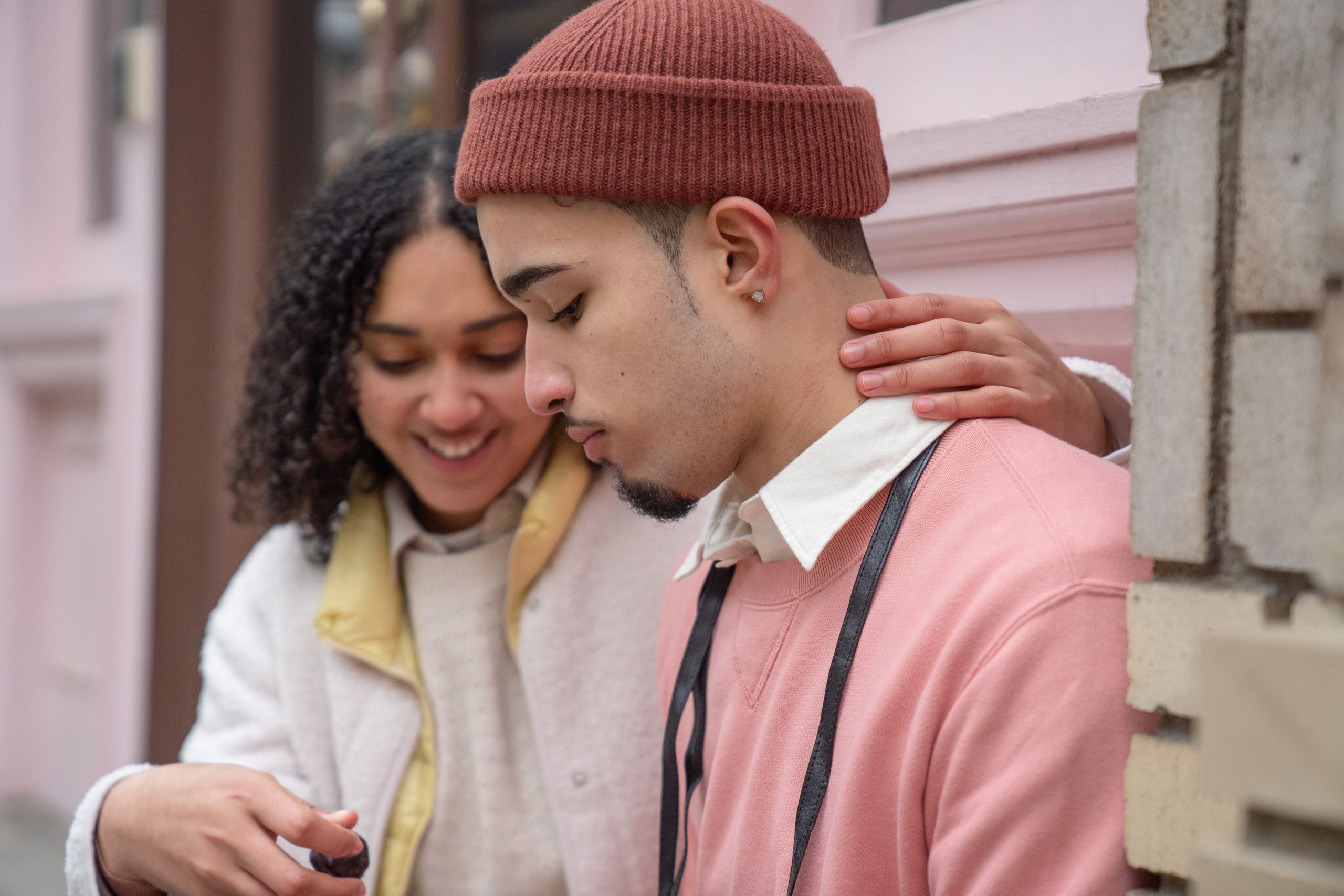 Positive Hispanic couple hugging and eating sweet chocolate candy while sitting on street near building in city during romantic date