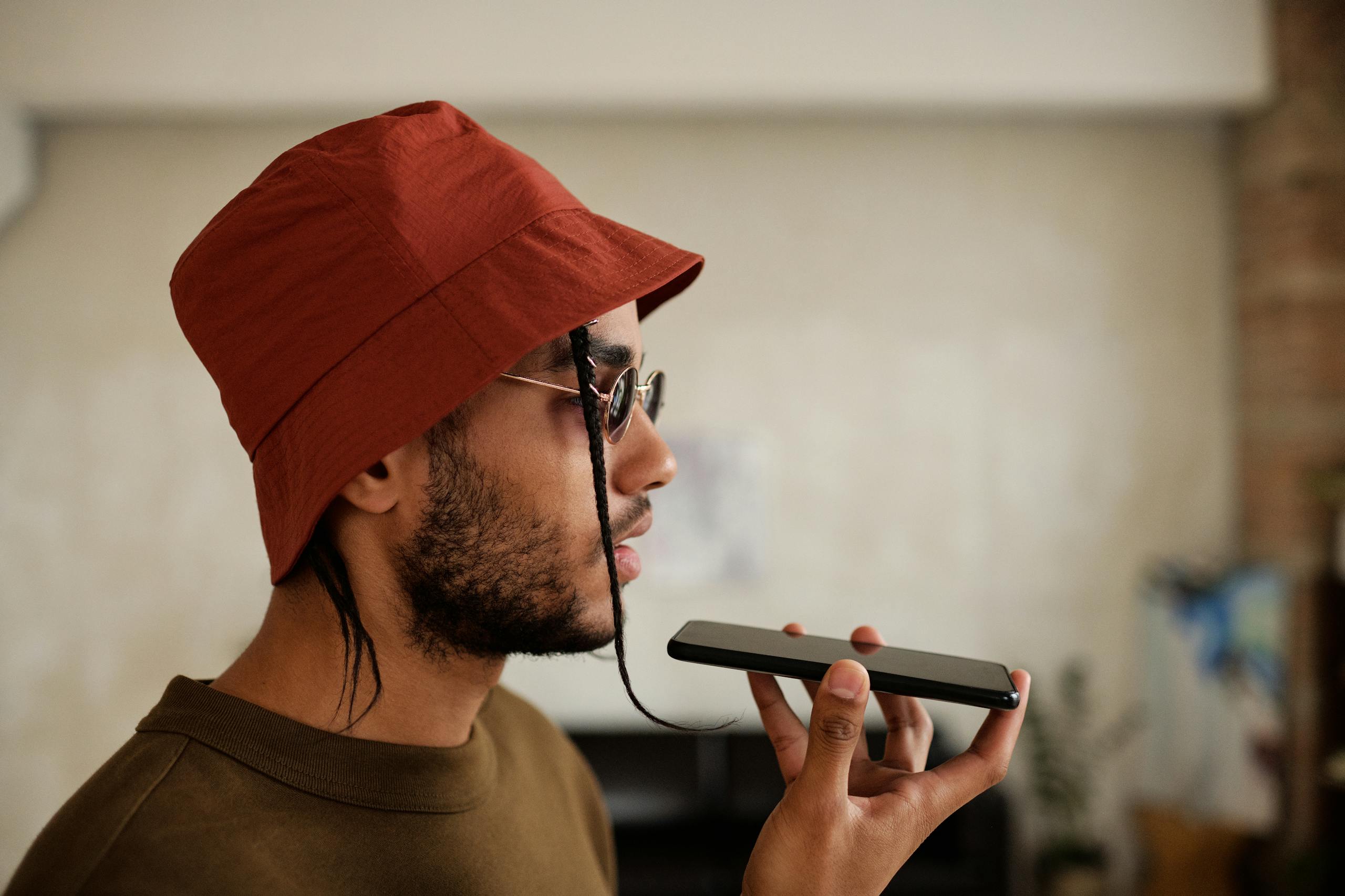 Profile view of a man in a red bucket hat talking on a smartphone indoors.