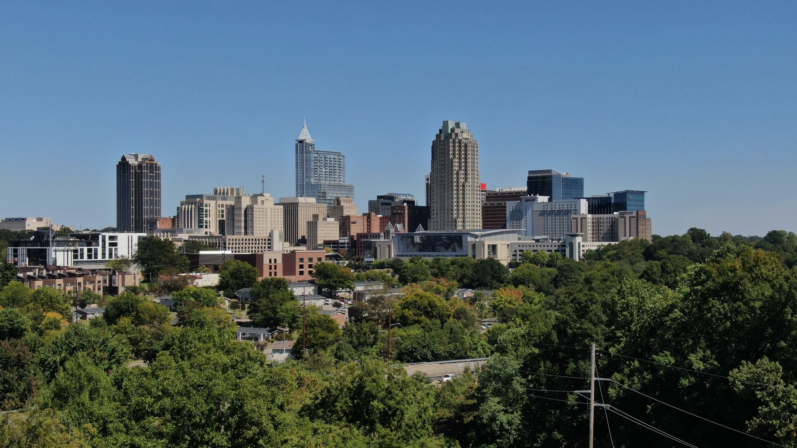 The Raleigh, NC skyline featuring modern architecture and lush greenery on a clear day.