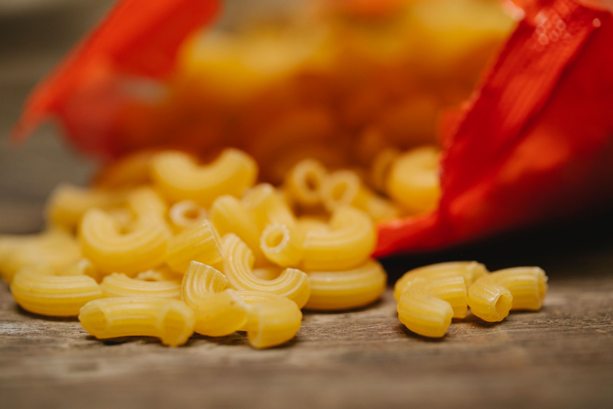 Raw uncooked pipe rigate pasta scattered on wooden table from pack before preparing dinner