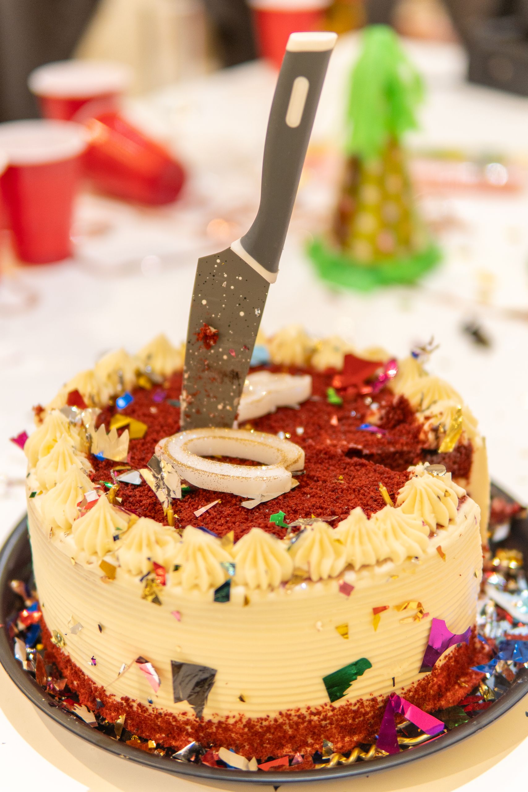 Red velvet cake with knife on top, surrounded by party decor.