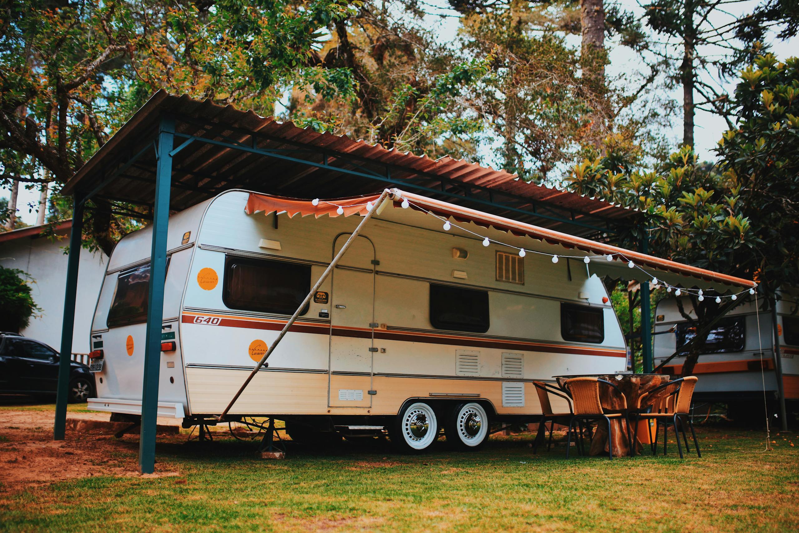 Relaxing motorhome camping setup with chairs and table in a scenic summer forest setting.