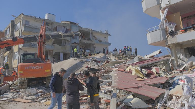 Rescue workers and machinery at an earthquake site showing damaged buildings and debris.