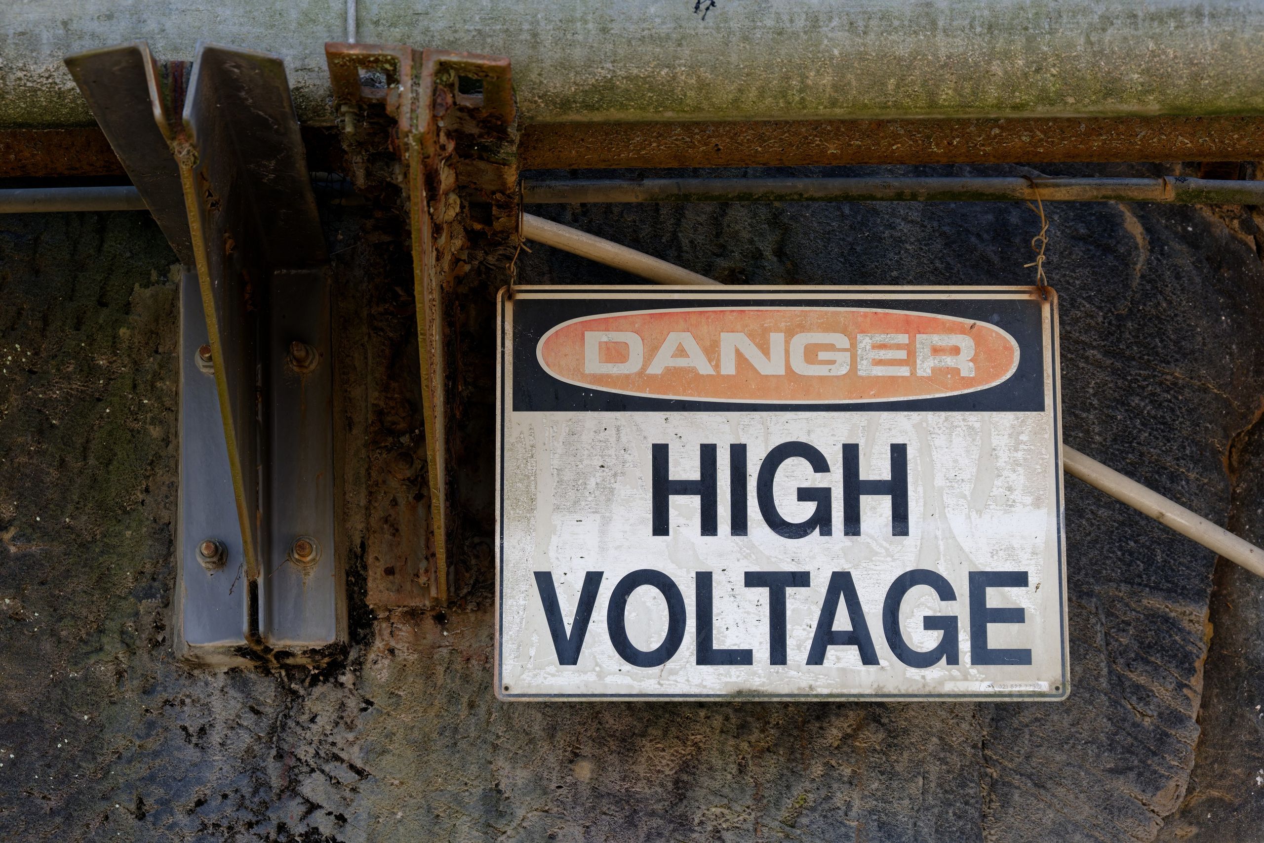 Rusty 'Danger High Voltage' sign on an outdoor wall, indicating electrical hazard.