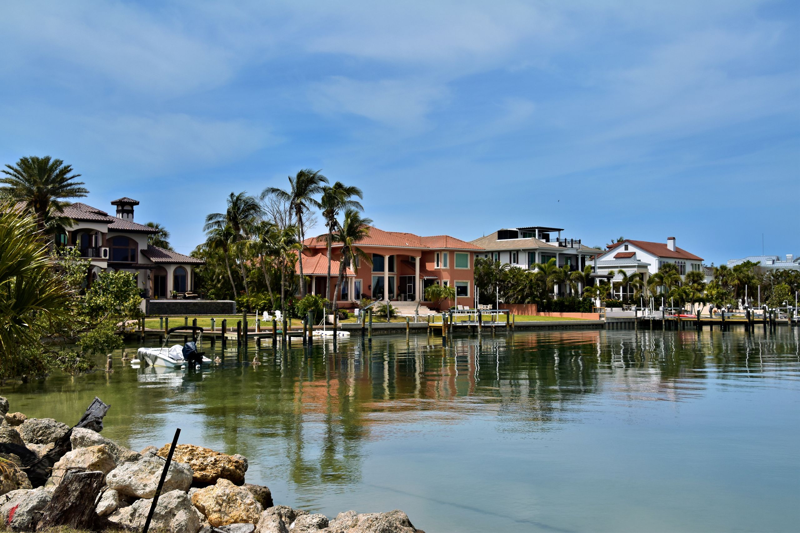 Scenic view of luxury homes along the Sarasota waterfront, surrounded by palm trees and calm waters.