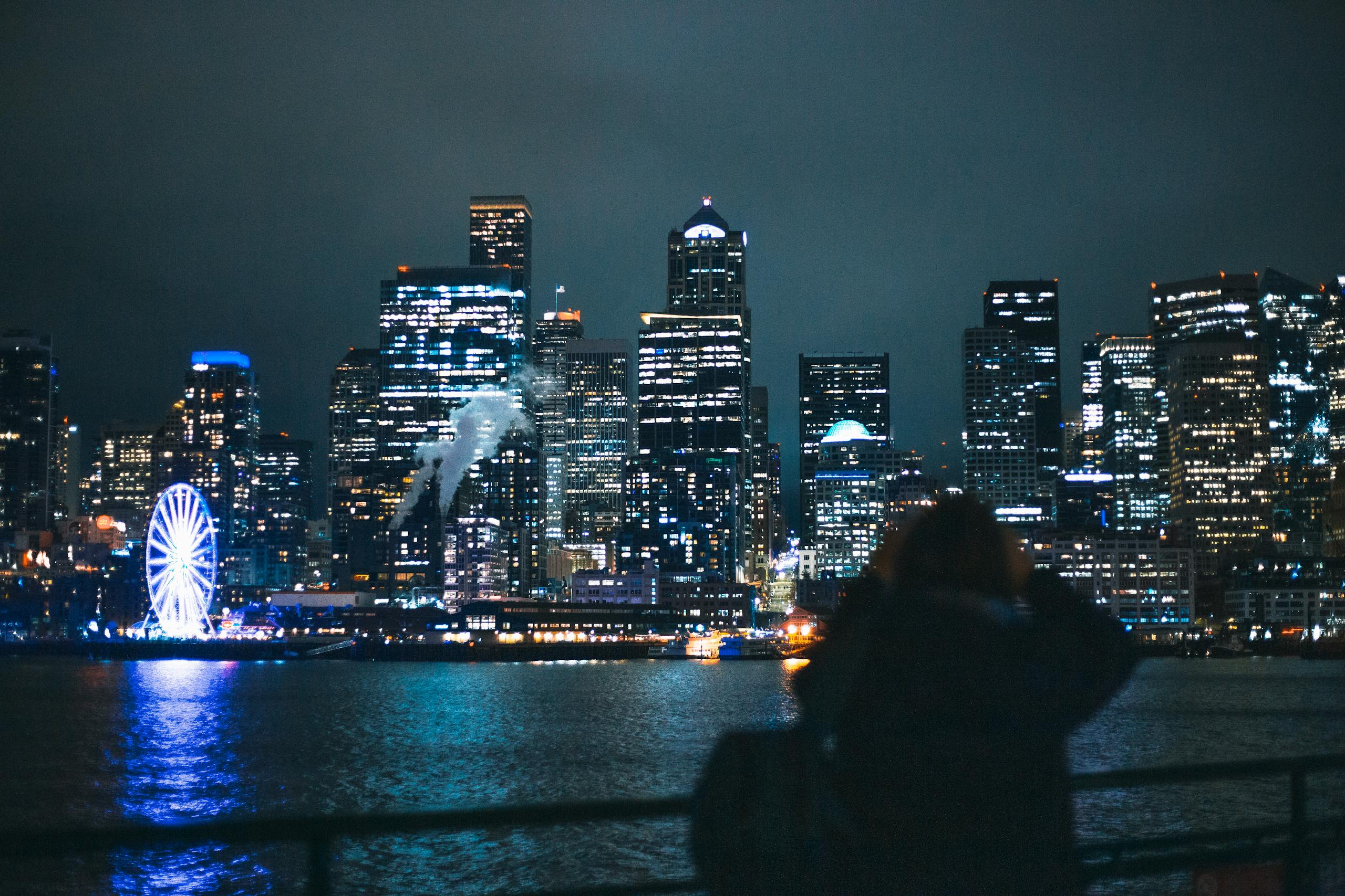 Scenic view of Seattle's skyline and Ferris Wheel at night, reflecting over water.