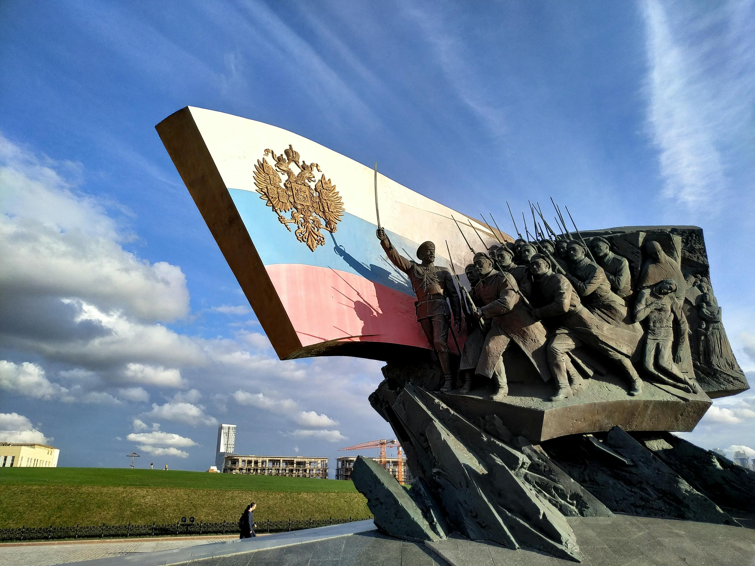 Sculptural monument depicting Russian soldiers with a patriotic flag against a blue sky.