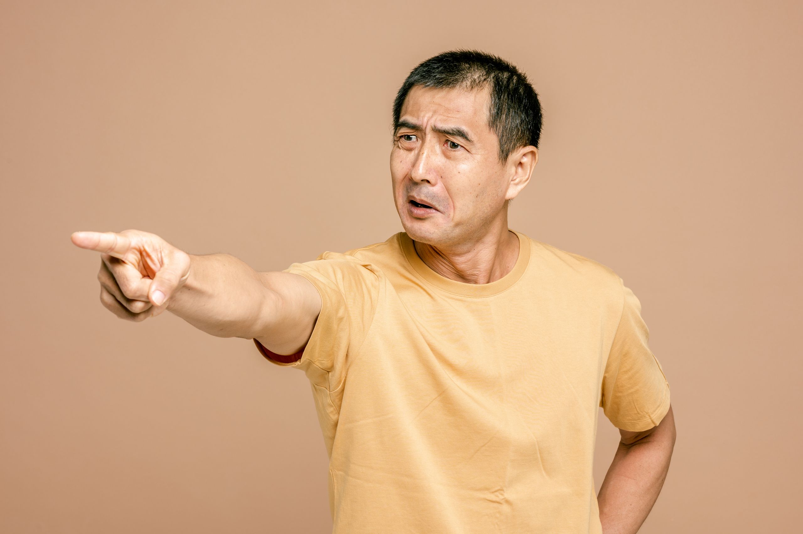 Senior Asian man expressing anger and pointing on a brown background.