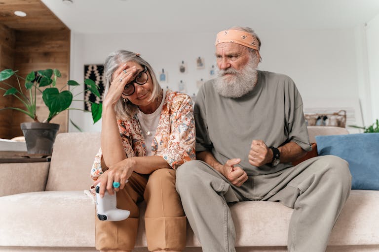 Senior couple expressing frustration while sitting on sofa indoors.