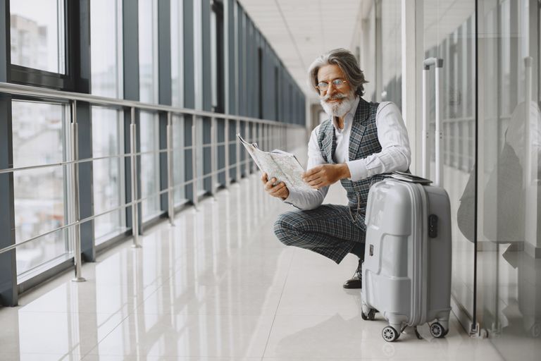 Senior man in airport hallway holding a map, sitting beside luggage, illustrating travel and exploration.