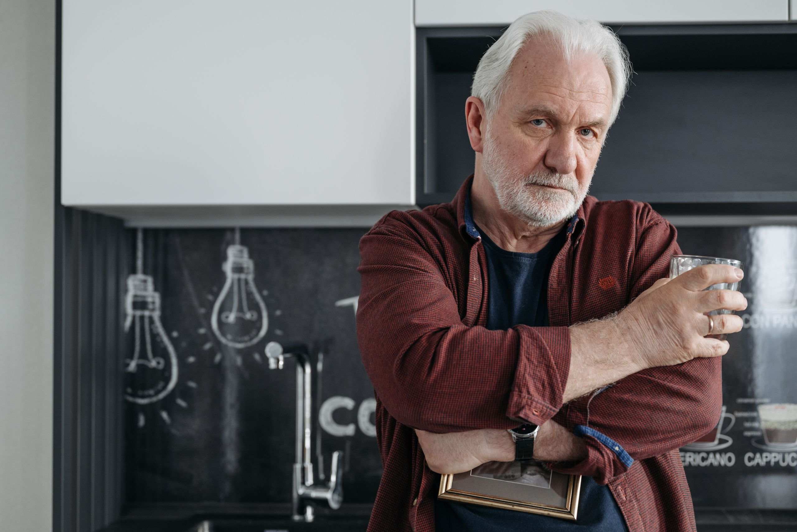 Senior man with gray hair holding a drink in a modern kitchen setting.
