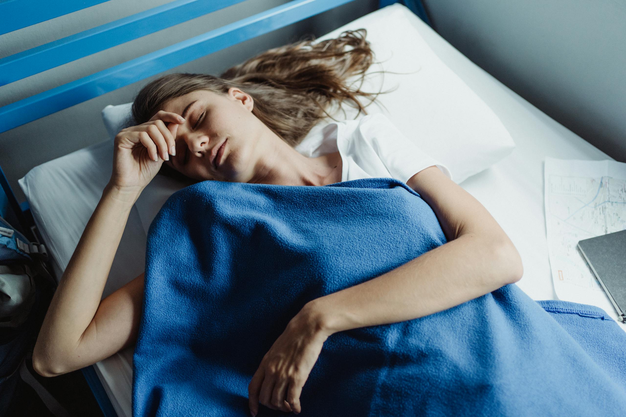 Serene daytime scene of a woman resting in bed wrapped in a blue blanket.