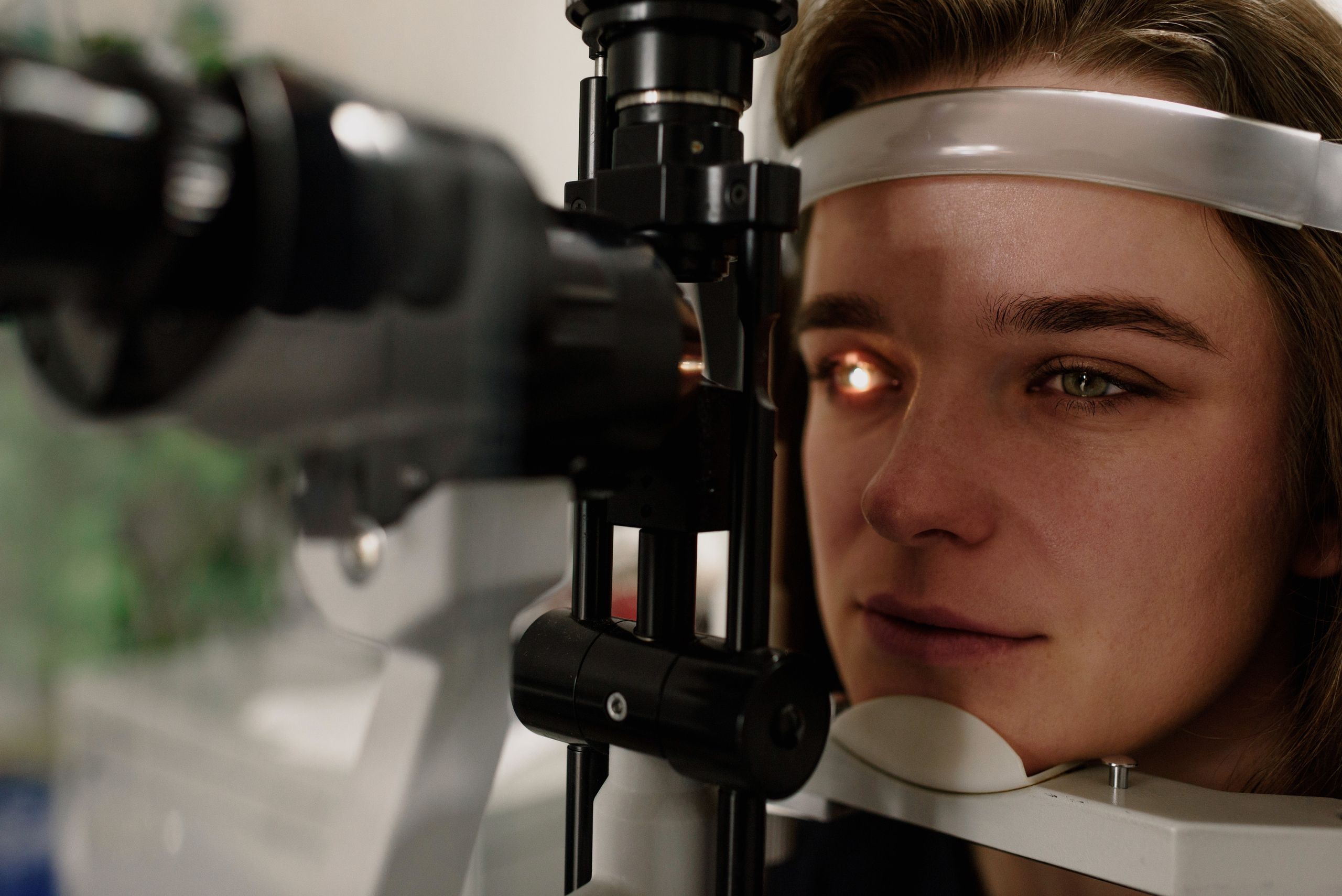 A serious female patient looking at light from contemporary ophthalmic bio microscope while getting eyesight examination in modern clinic during a checkup.