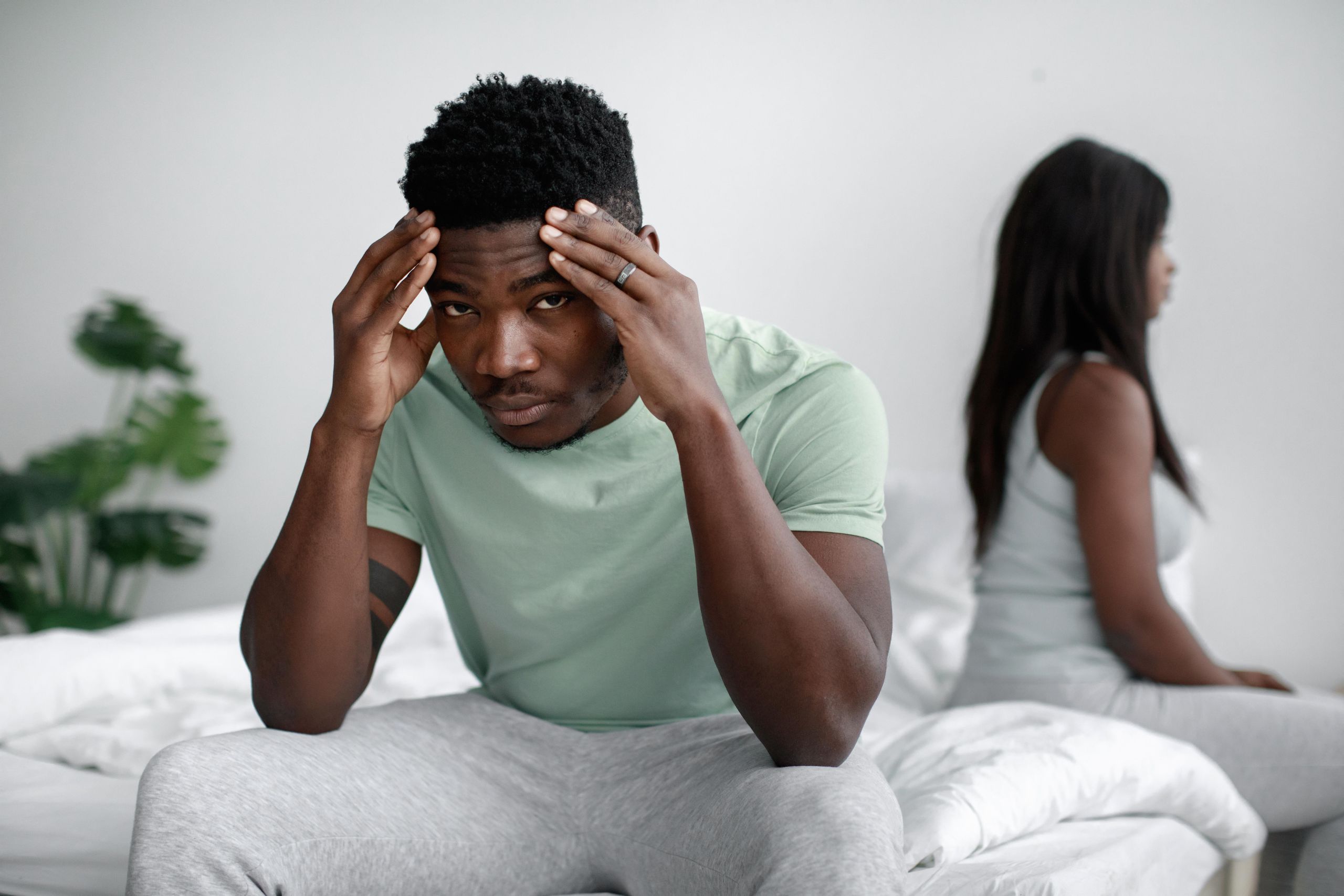 Serious moment between an African American couple sitting in a bedroom, highlighting relationship tension.
