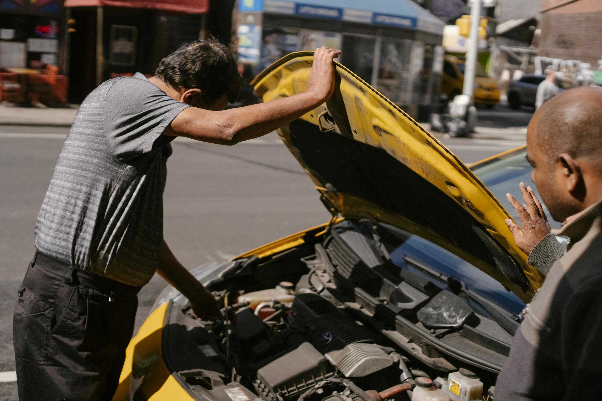 Side view of ethnic men repairing detail of engine in damaged car parked on roadside