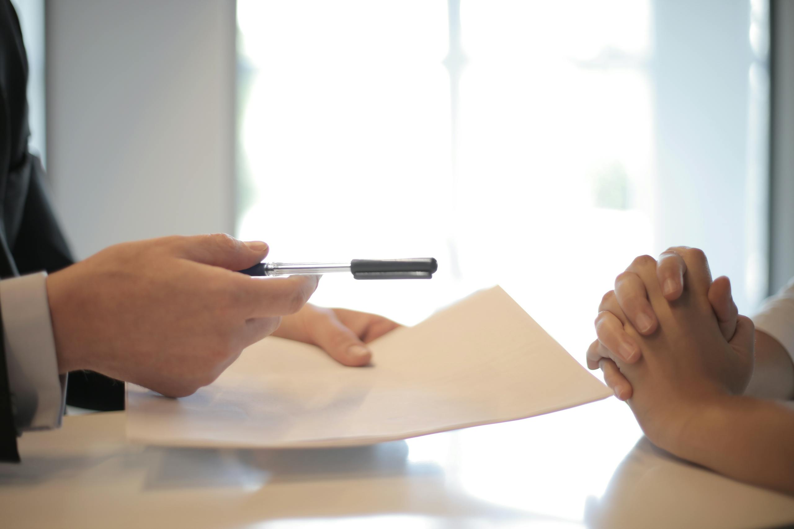 Side view of faceless formal man giving pen and paper to focused female with clenched hands at table on meeting