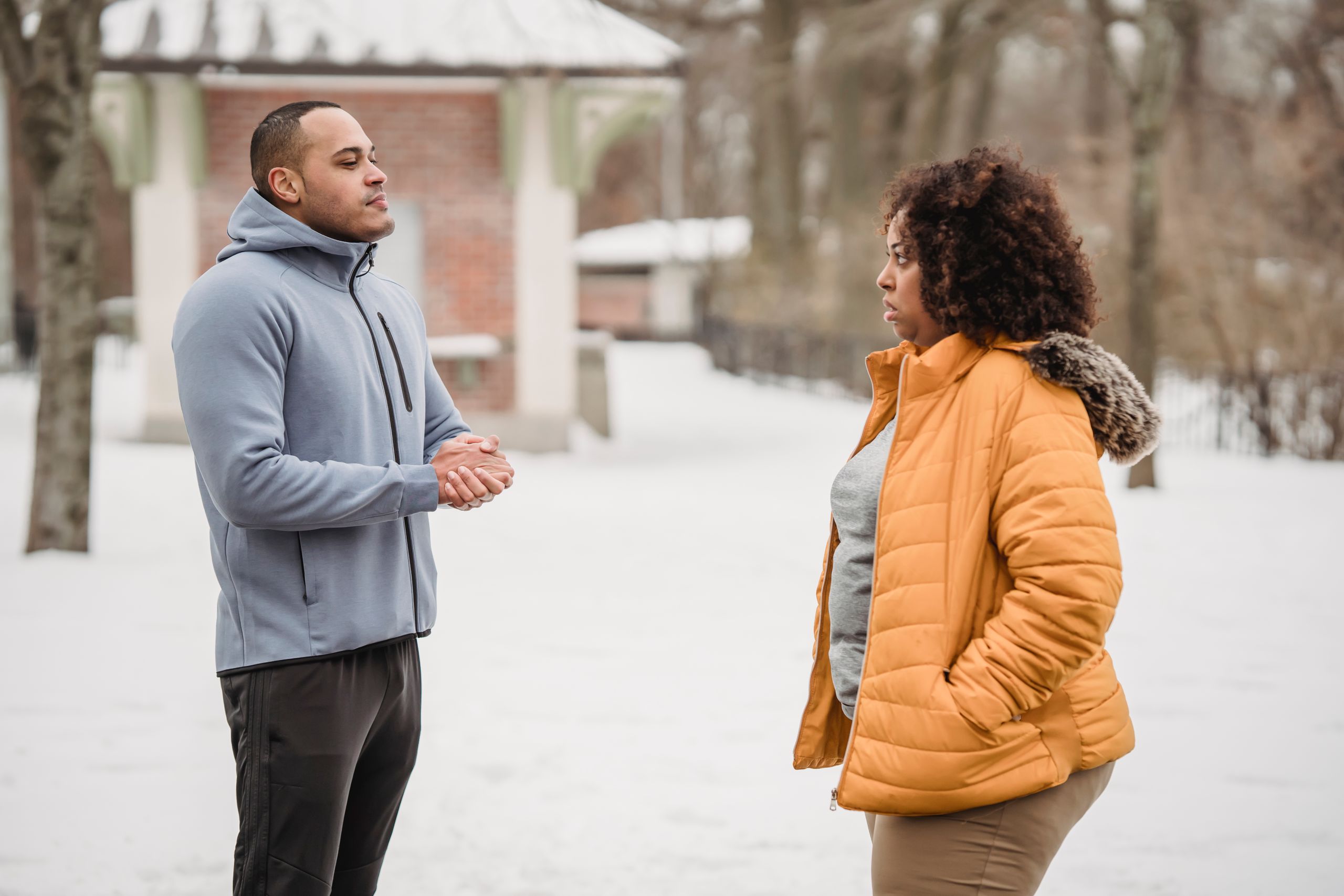 Side view of plump African American and black man in sportswear looking at each other while standing on snowy ground during workout