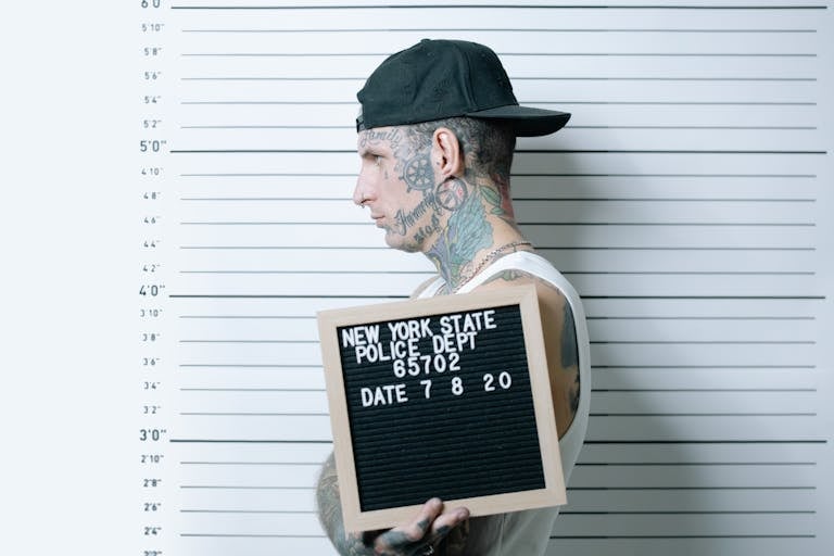Side view of tattooed man holding mugshot board in police lineup.
