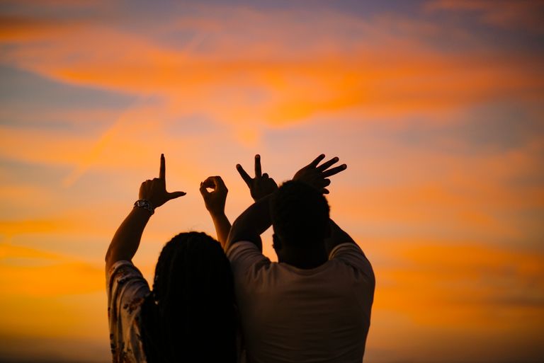 Silhouetted couple expressing love through hand gestures against a vibrant sunset sky.