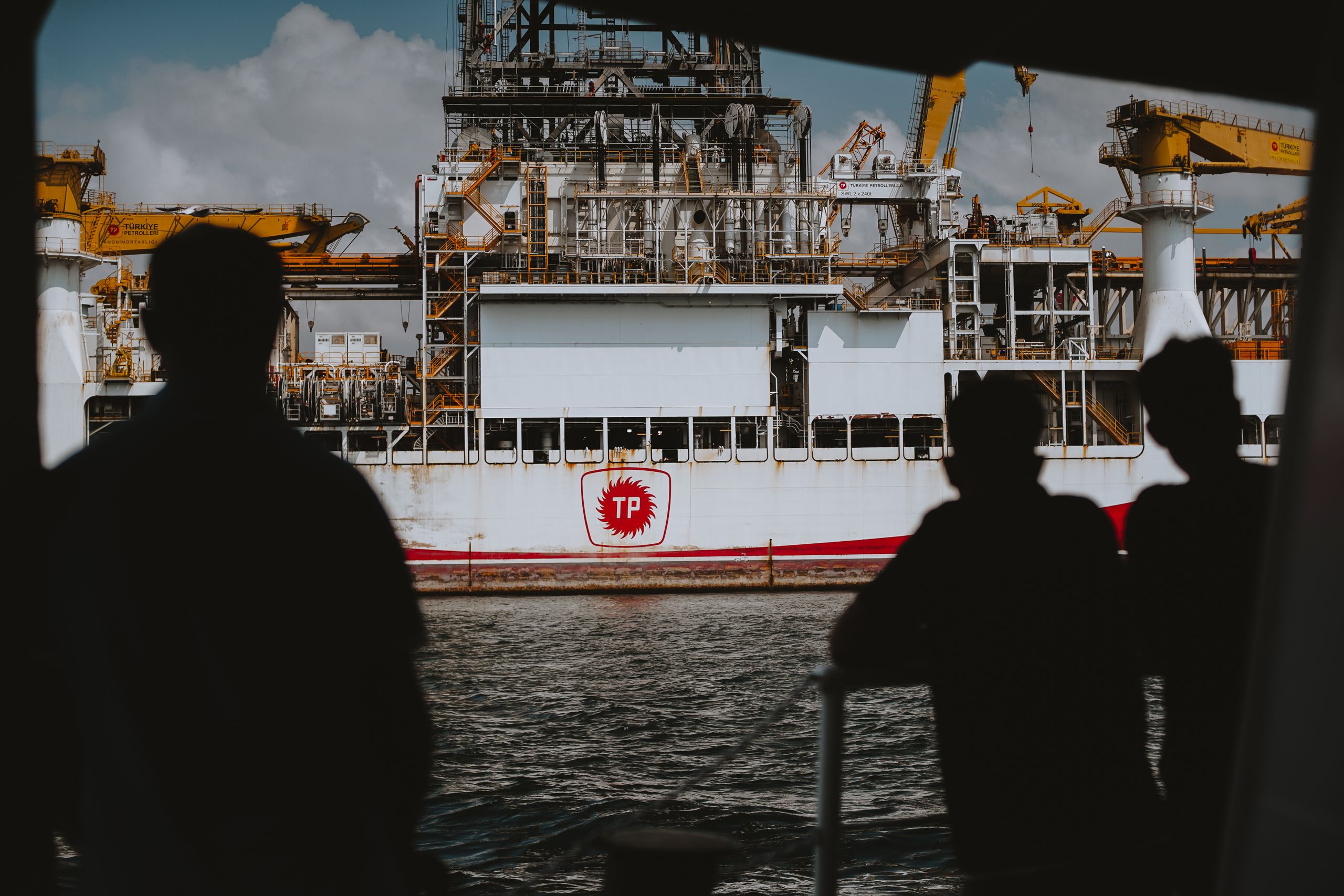 Silhouetted figures observing a large offshore oil rig at sea, emphasizing maritime industry.