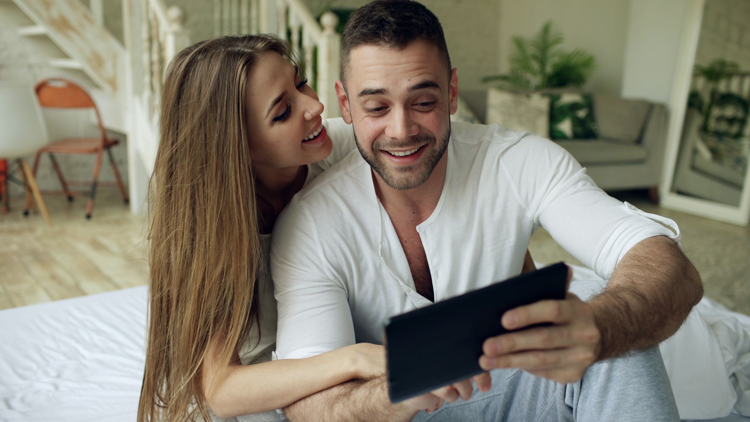 Smiling couple taking a cheerful selfie together indoors on a cozy morning.