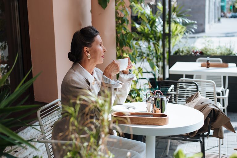 Sophisticated woman in an outdoor café savoring coffee. Bright and serene atmosphere.