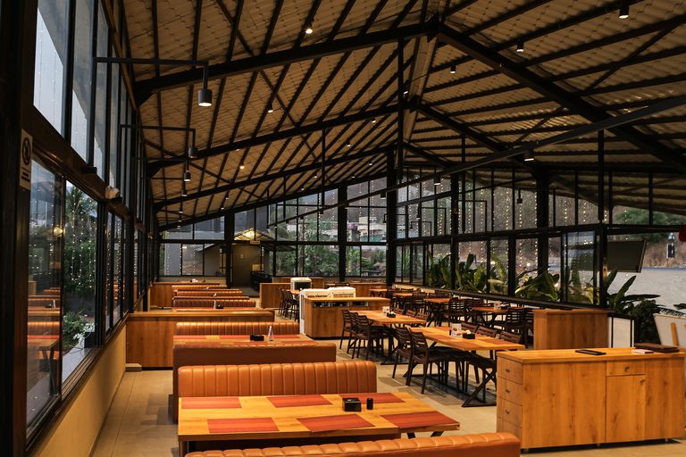 Spacious modern restaurant interior with glass walls and stylish wooden furniture featuring ambient lighting.