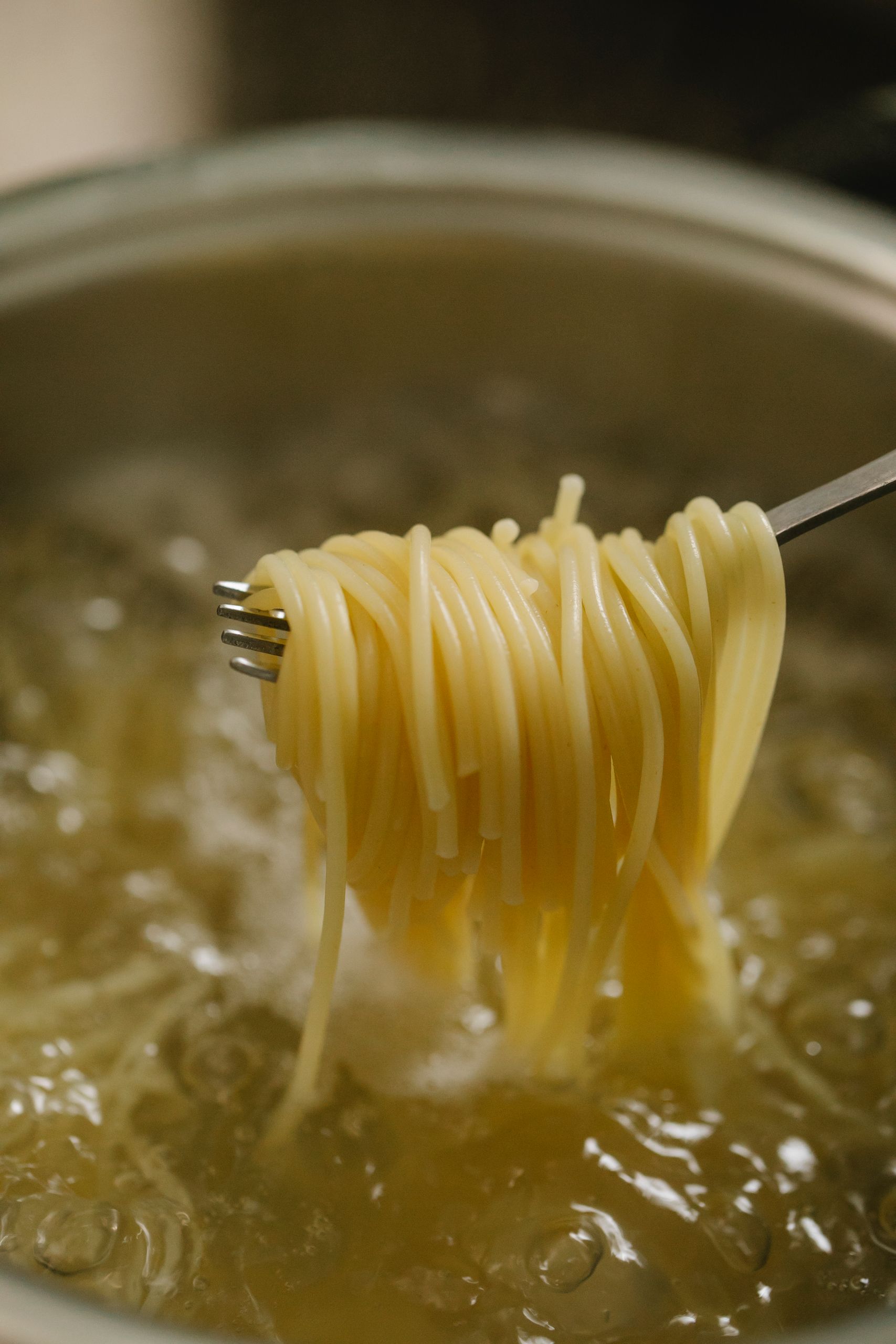 Spaghetti around fork placed above saucepan with pasta cooking in boiling water in light kitchen