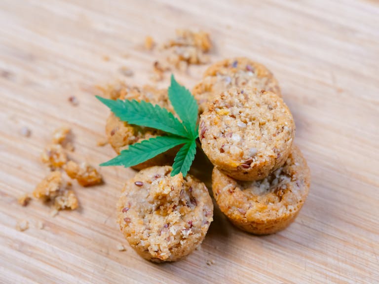 Stack of cannabis-infused muffins with a cannabis leaf on a wooden surface. Ideal for cannabis culture concepts.