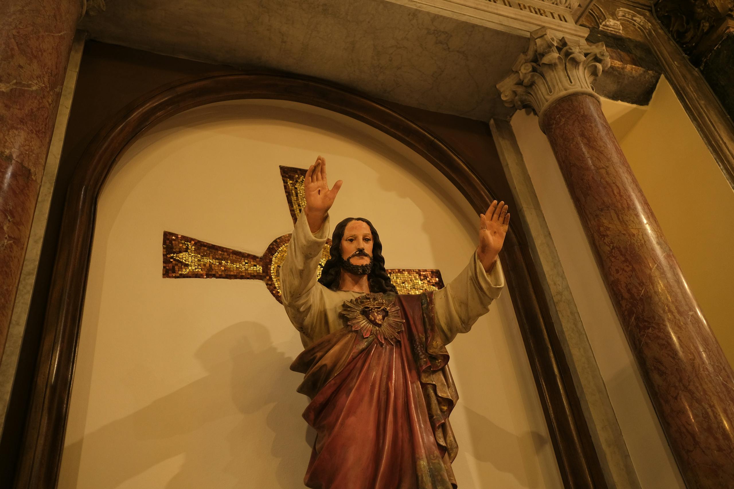 Statue of Jesus Christ with arms raised inside a church setting, emphasizing spirituality.