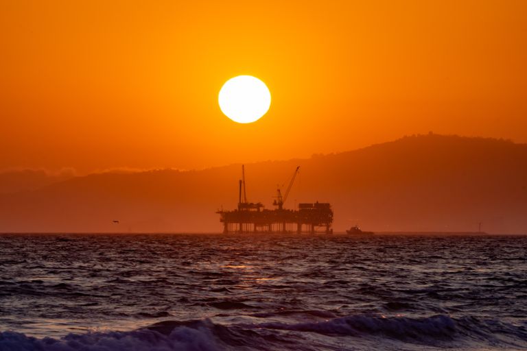 Stunning view of a silhouetted oil platform against a vibrant orange sunset over Huntington Beach, California.