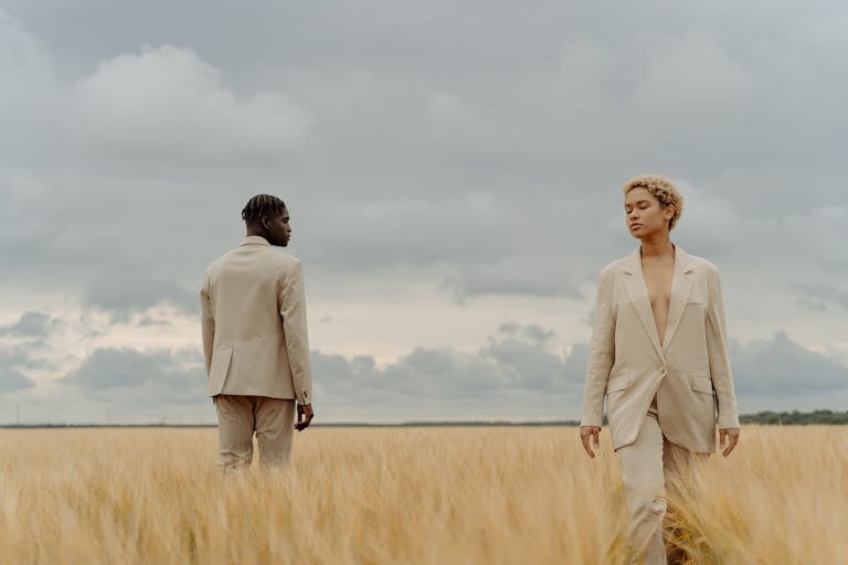 Stylish individuals in suits posing in a serene meadow under a cloudy sky.