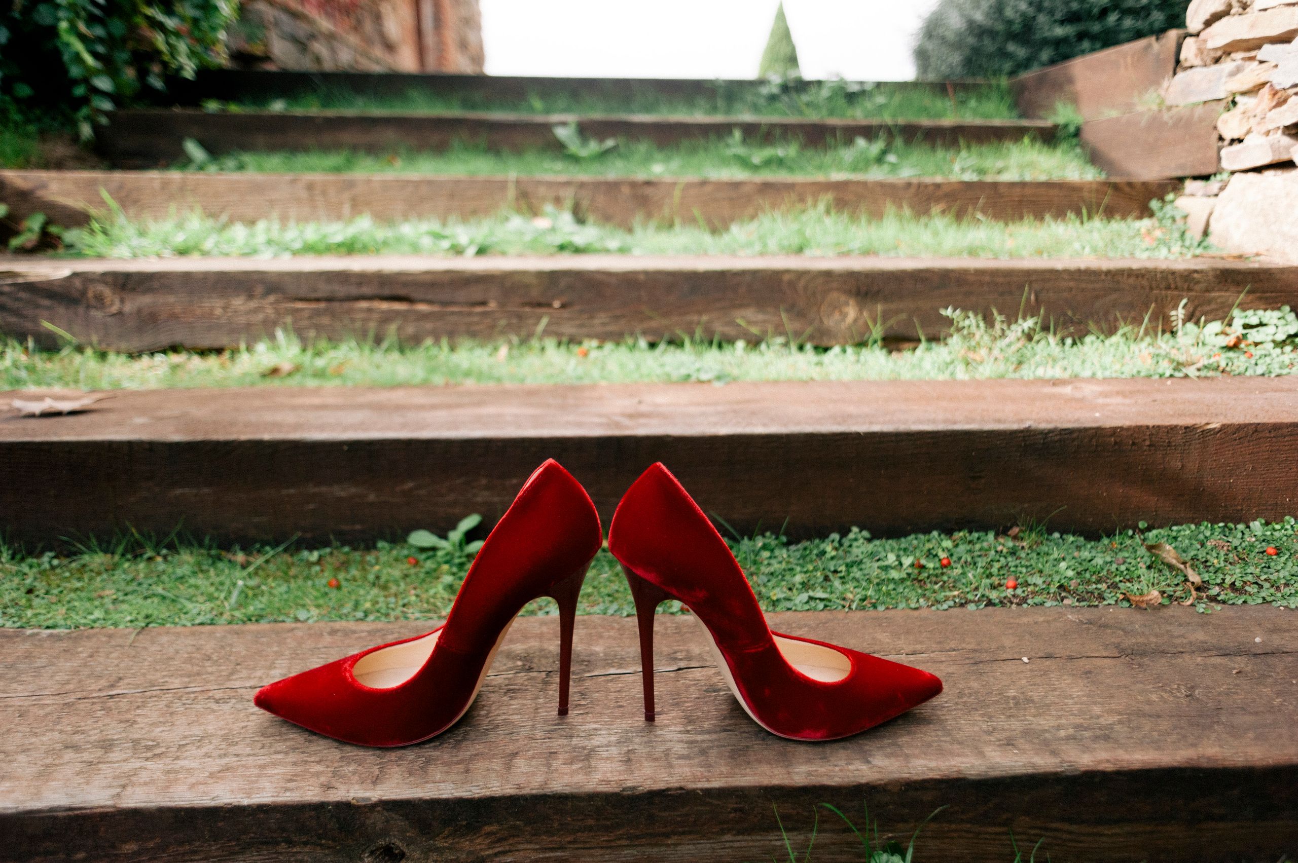 Stylish red velvet high heels placed on wooden steps outdoors, perfect for fashion and lifestyle themes.