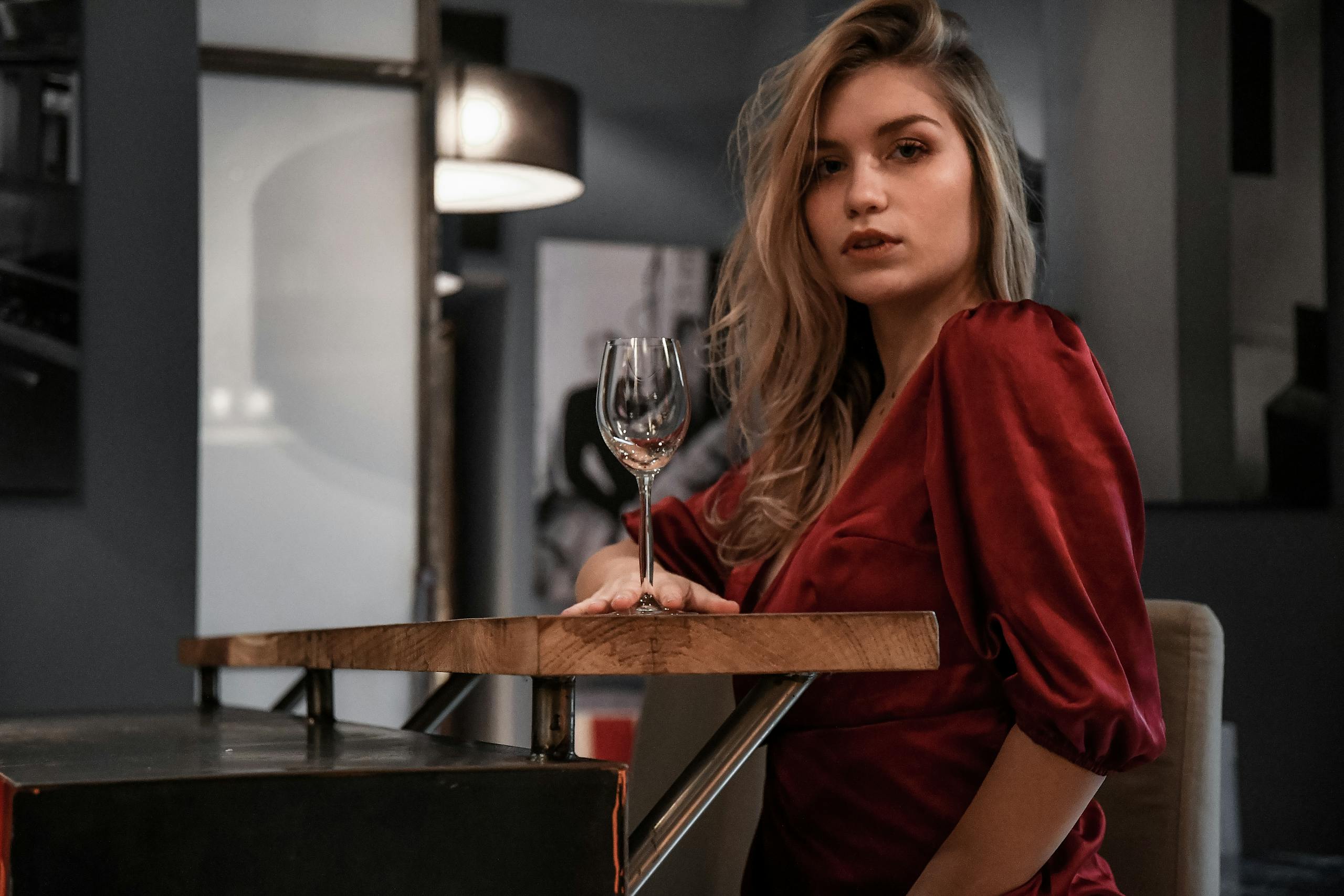 Stylish woman in red pose elegantly with an empty wine glass indoors.