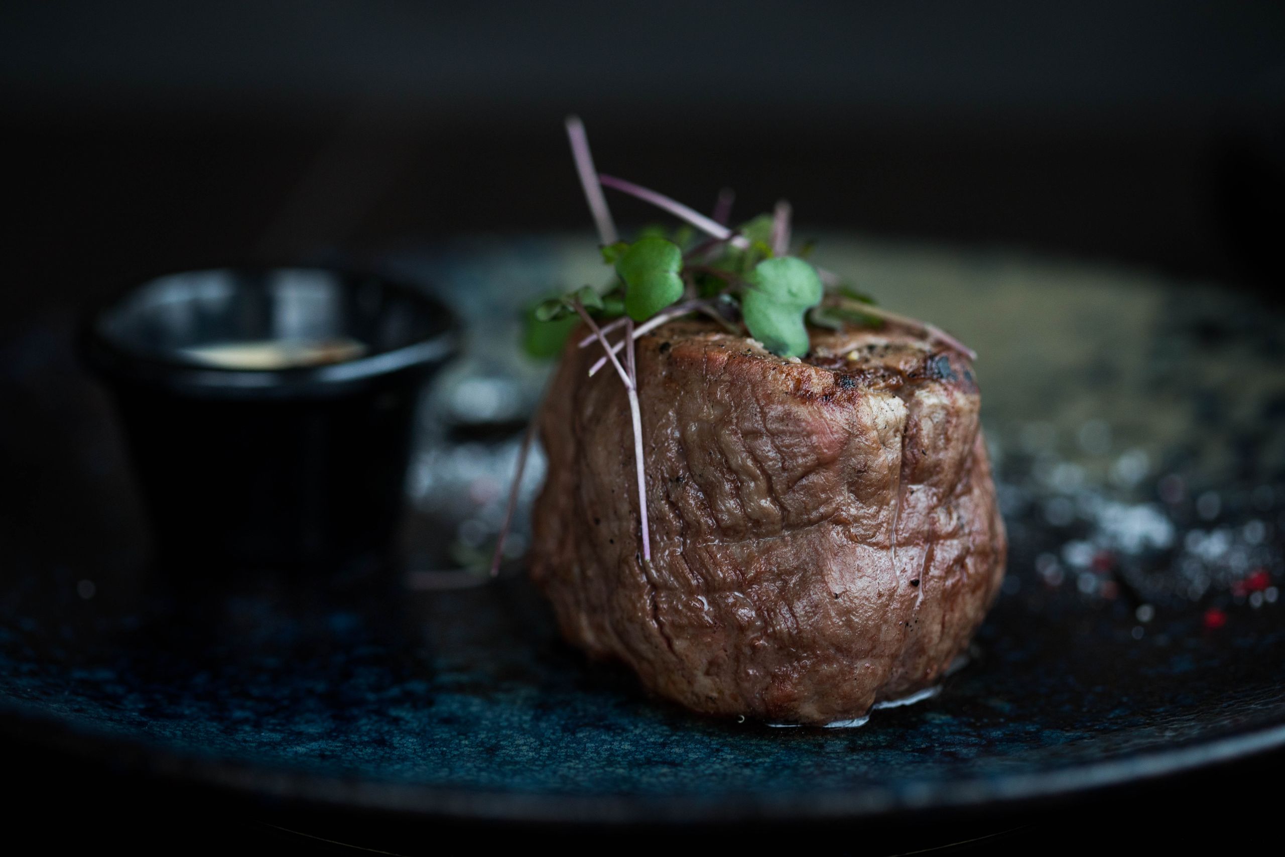 Succulent grilled steak topped with microgreens served on a dark plate for a gourmet meal.