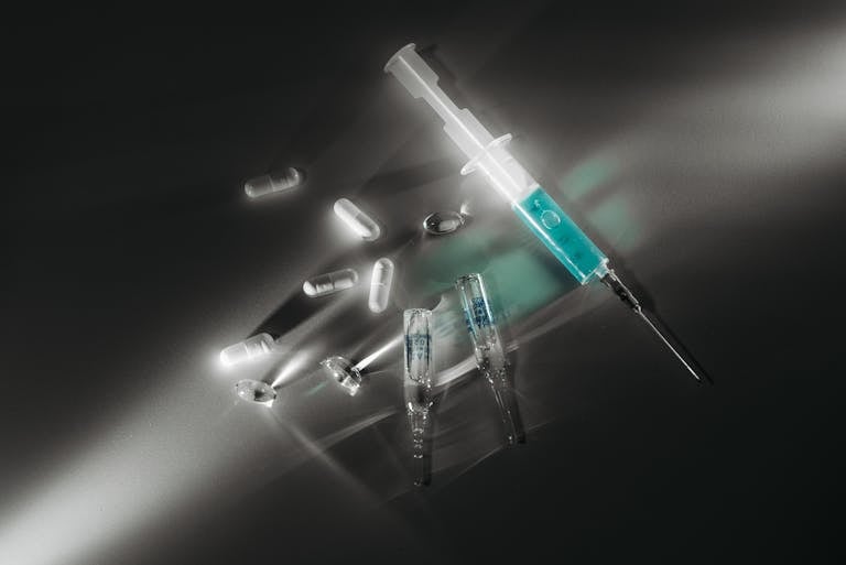 Syringe and medicine capsules illuminated in a dark, dramatic setting, emphasizing medical themes.