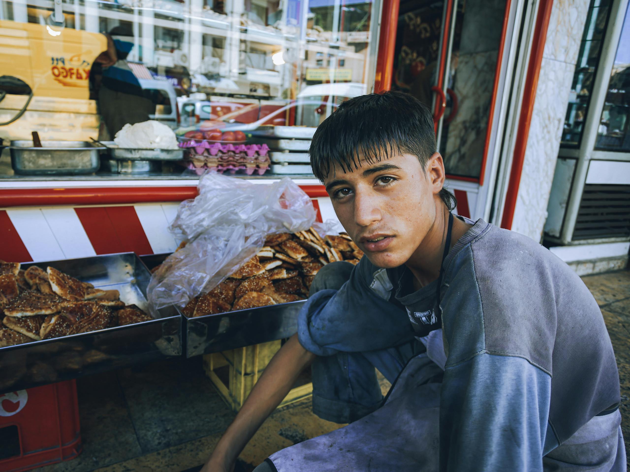 Teenage boy in casual clothing sitting beside a street pastry stall, showcasing urban commerce.