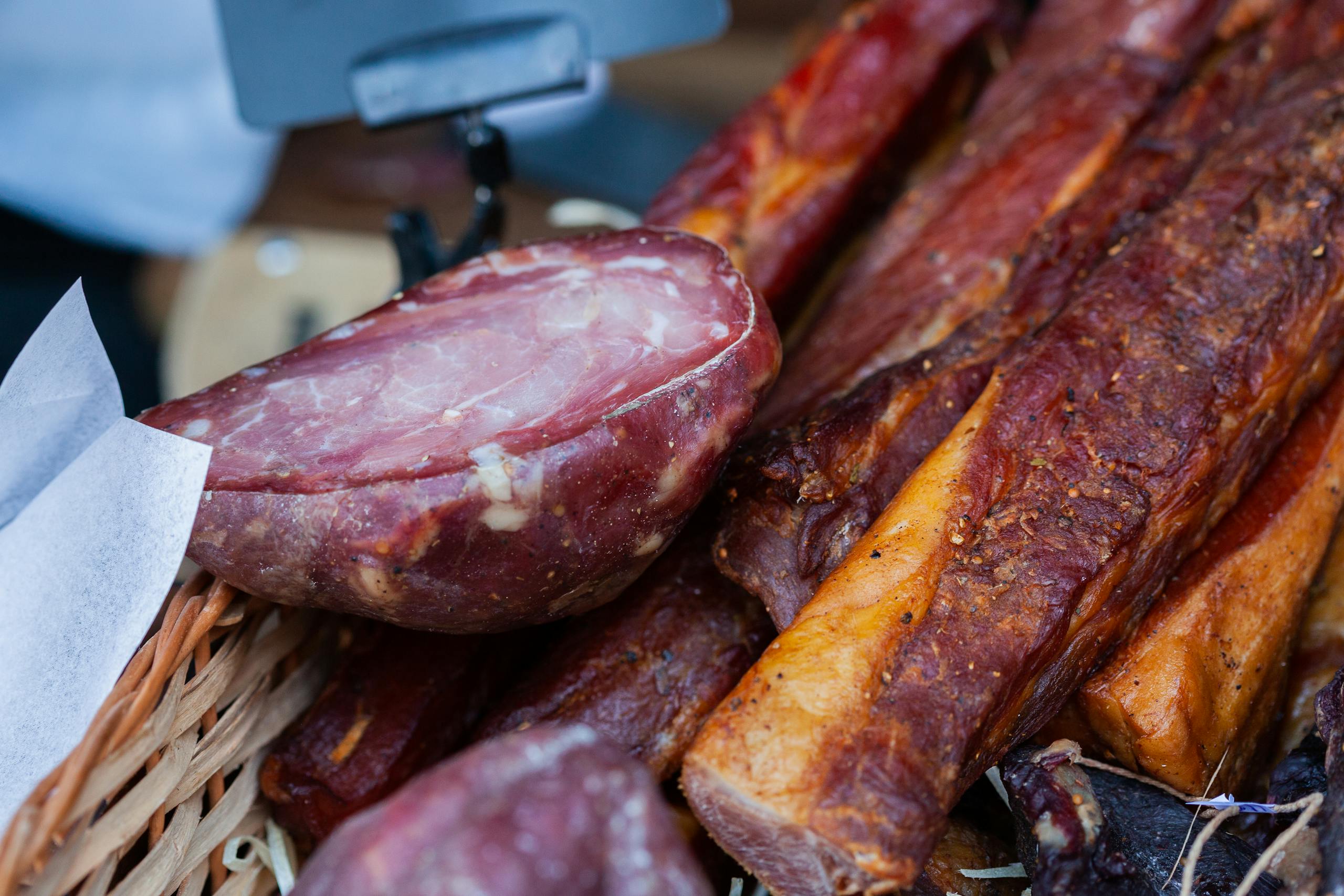 Tempting close-up of assorted smoked meats in a market basket, showcasing rich textures and flavors.