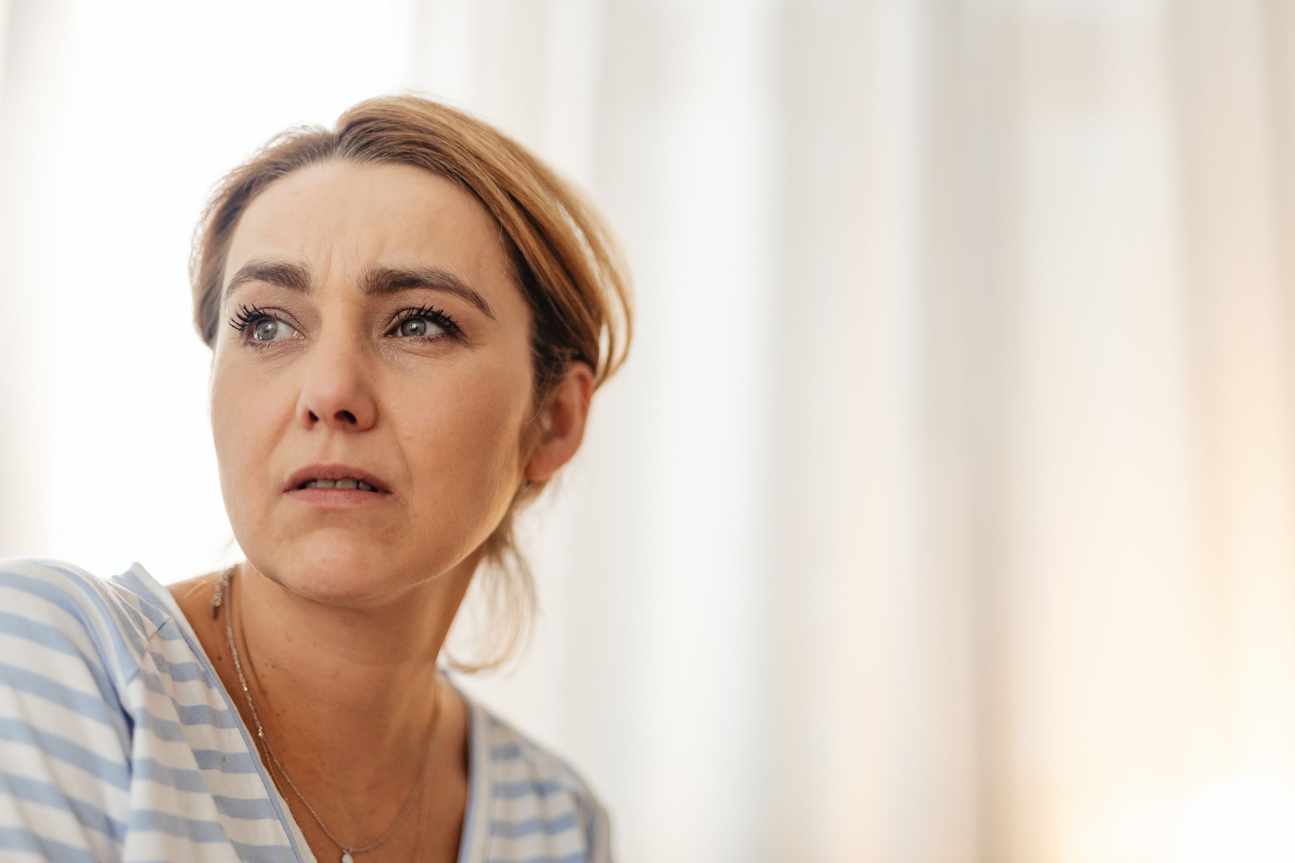 Thoughtful woman in striped shirt gazing away in gentle indoor lighting.