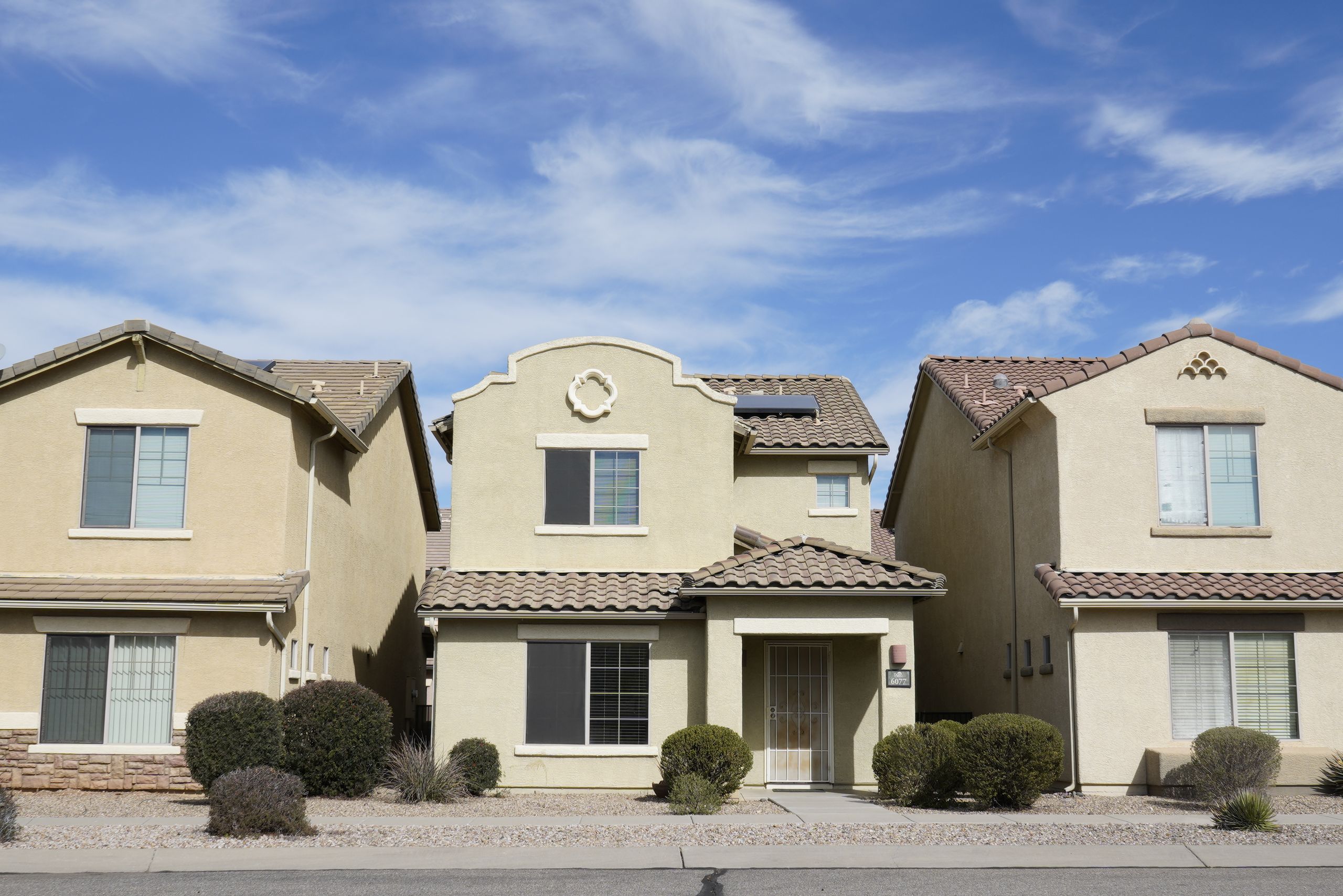 Three adjacent houses in a suburban neighborhood of Tucson, Arizona under a clear sky.