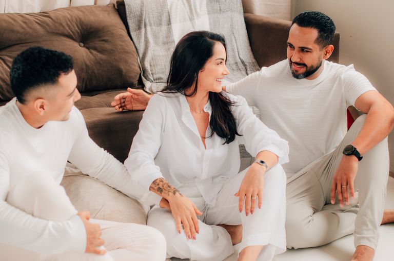 Three adults in casual attire having a relaxed conversation indoors.