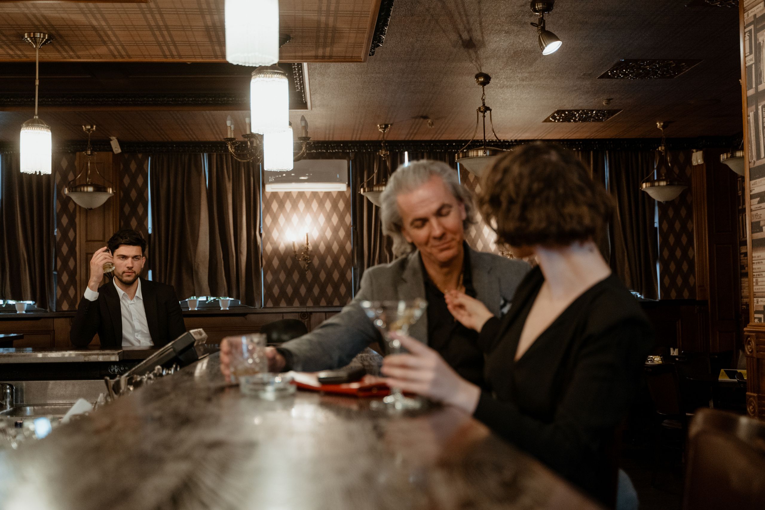 Three people enjoying drinks at a stylish, dimly lit bar, creating a warm atmosphere.