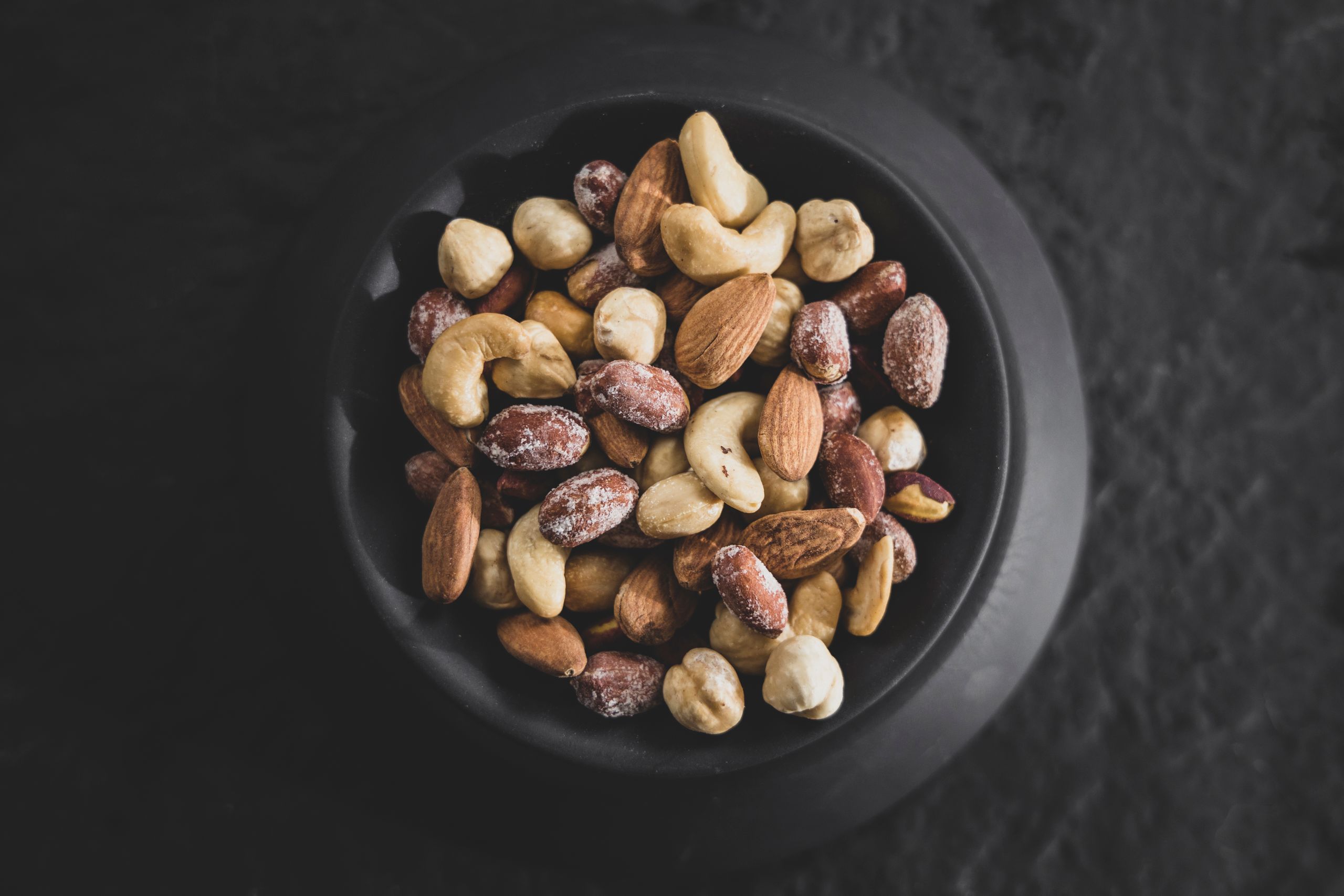 Top view of a variety of mixed nuts in a black bowl, showcasing almonds, cashews, and hazelnuts.