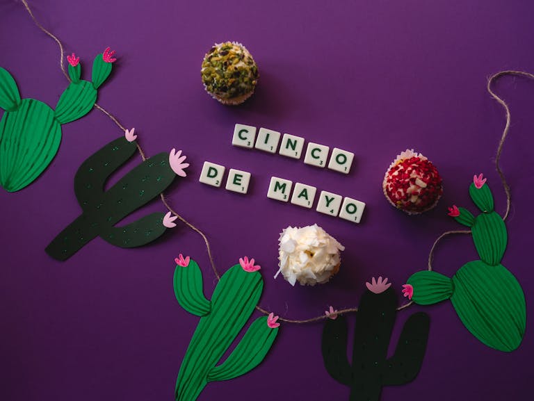 Top view of cupcakes and cactus decorations celebrating Cinco de Mayo with scrabble tiles.