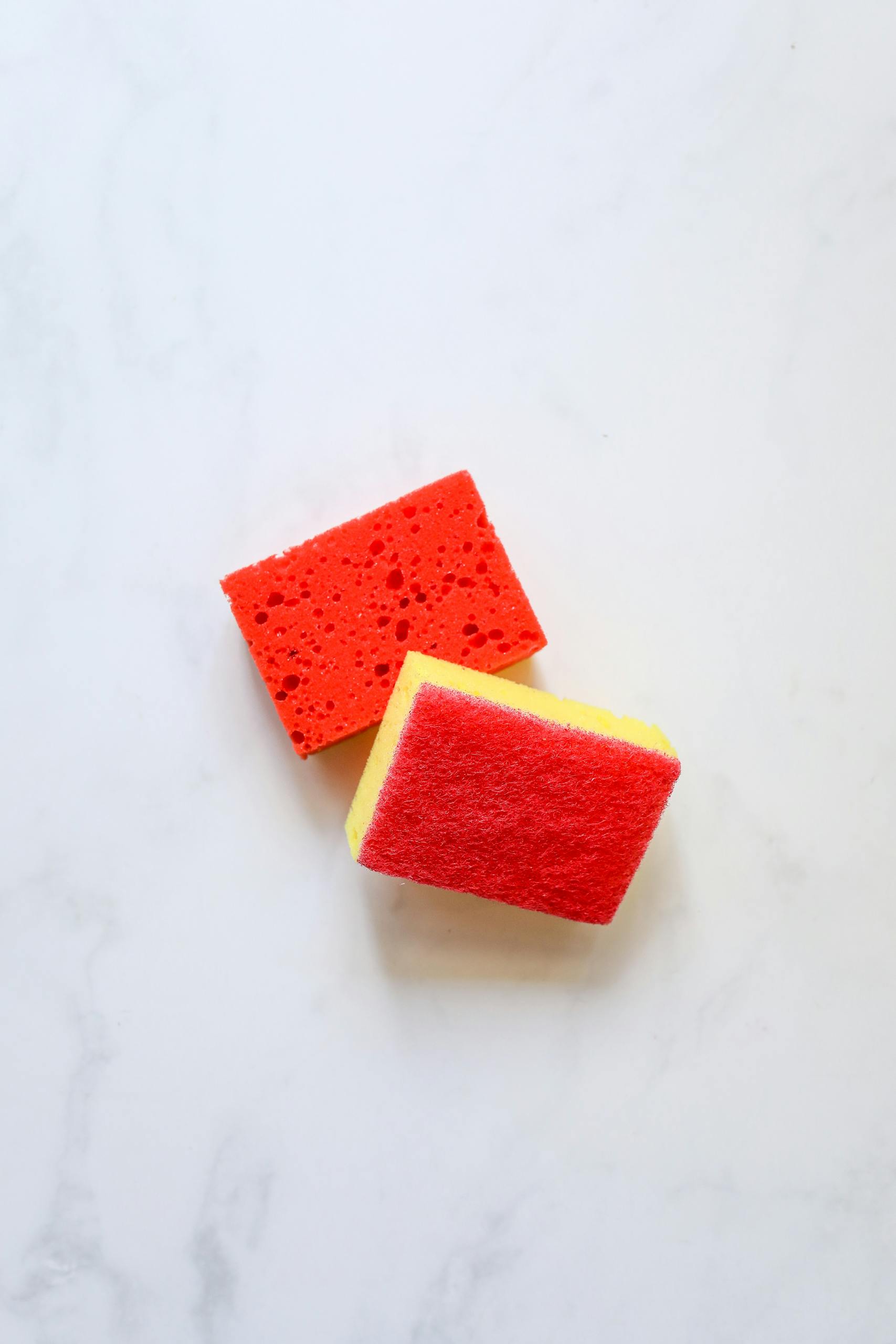 Top view of red and yellow cleaning sponges on a marble surface, perfect for housekeeping themes.