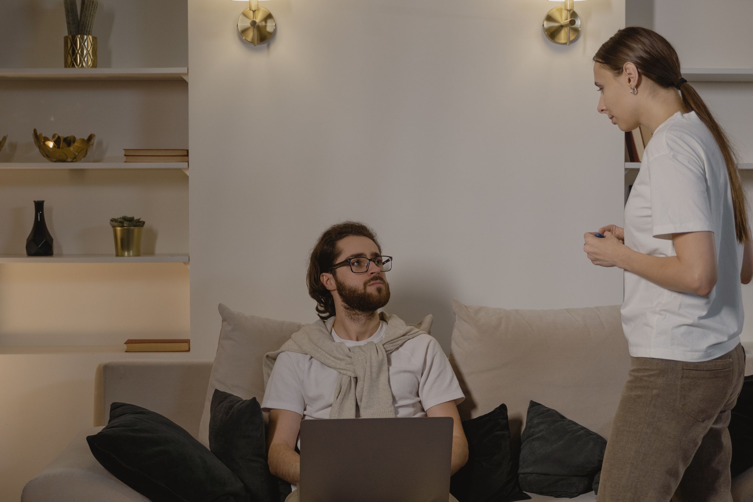 Two adults engage in a casual conversation indoors sitting on a sofa, creating a cozy ambiance.